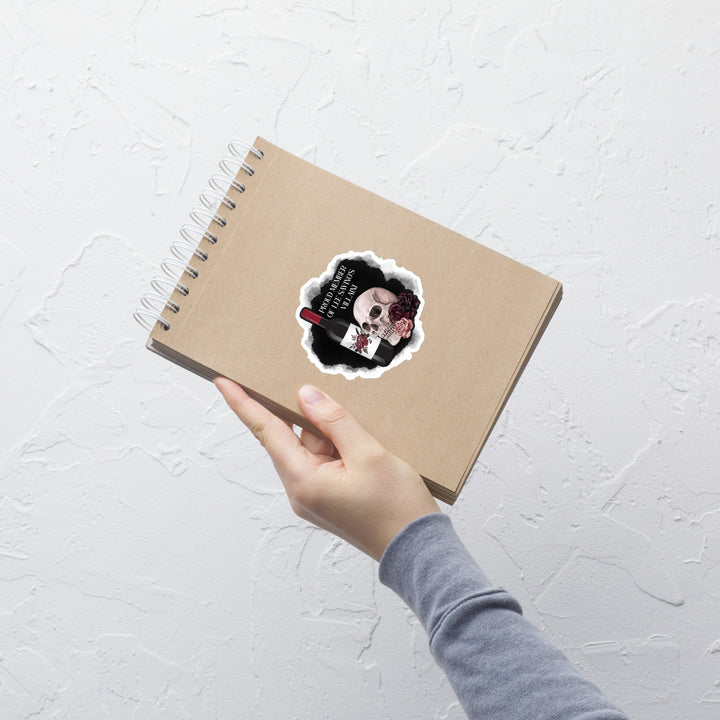 Hand holding a spiral-bound notebook with a sticker on a light gray textured surface
